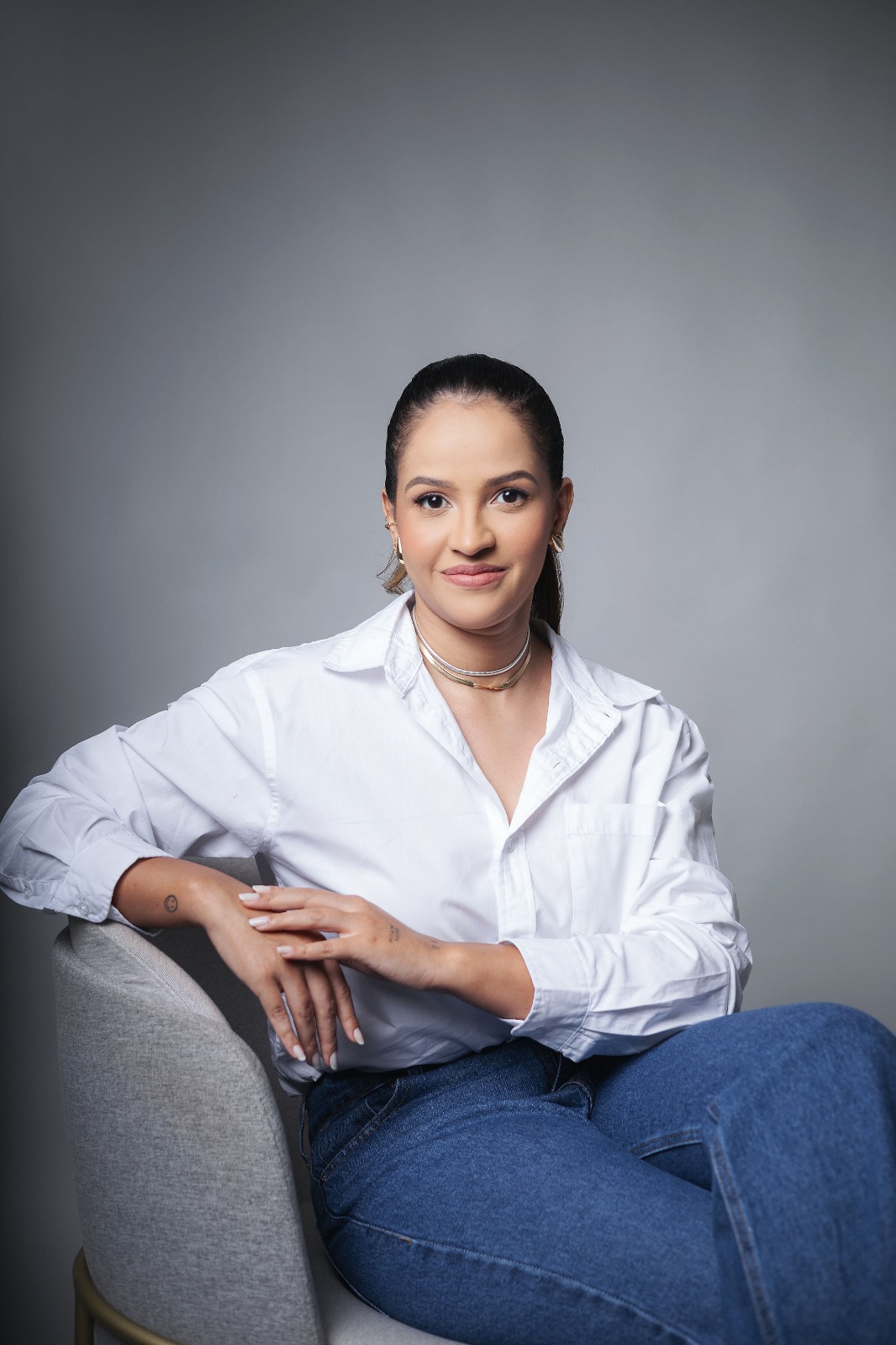 Foto profissional da nutricionista Apoena, sentada em poltrona clara, sorrindo